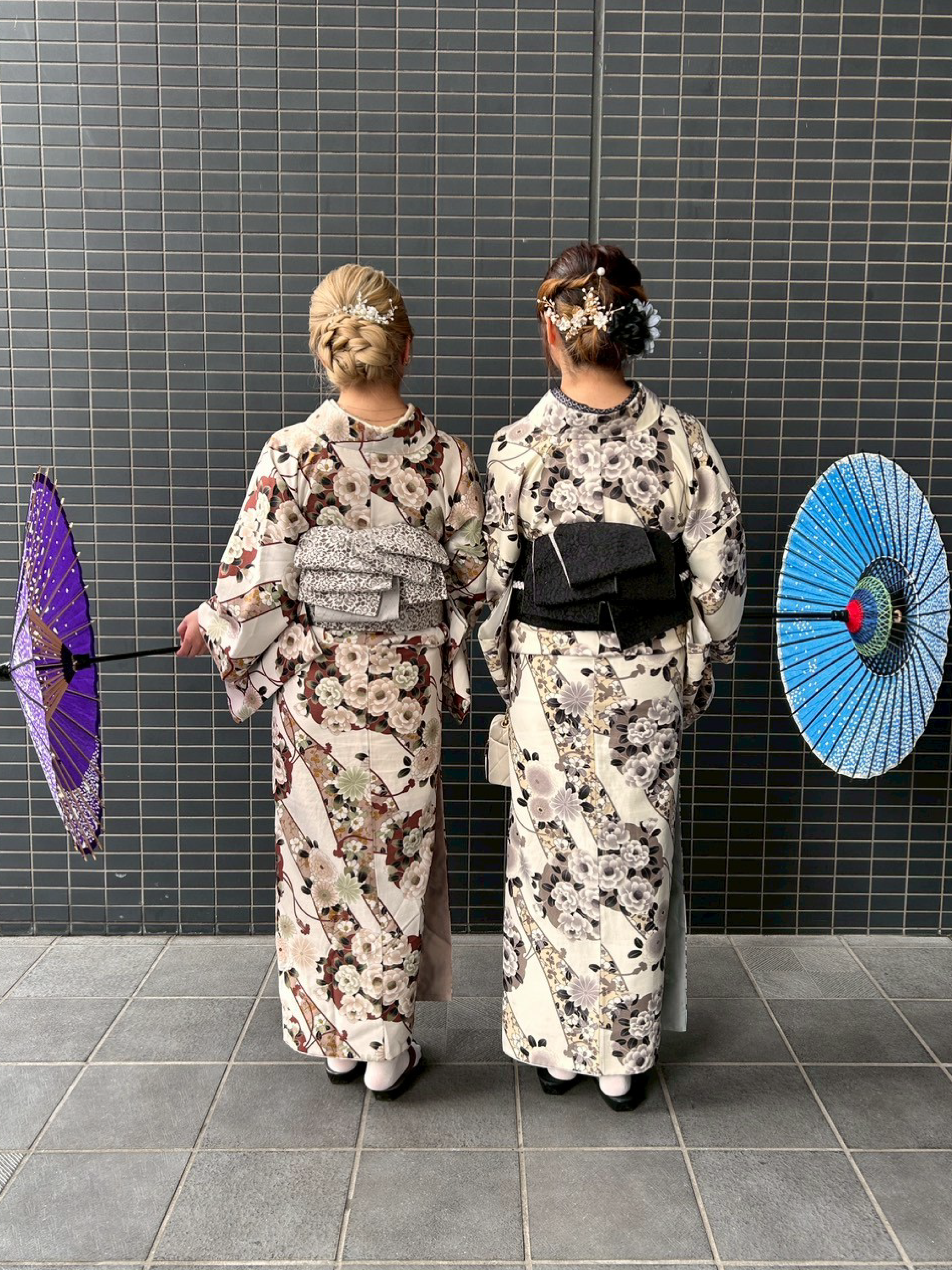 和傘もった後ろ姿の女性二人組。茶系とグレー系の色味の着物を各々着用