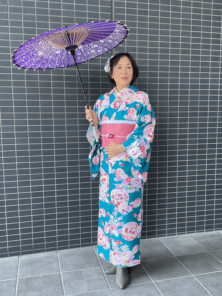 鮮やかなピンクと紫の花柄・黒地の着物を着用した女性。店舗にある撮影グッズの和傘を持って記念撮影